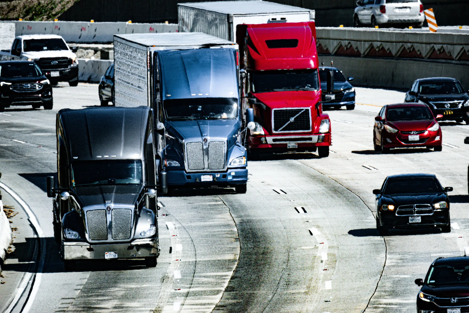 Conventional semi-trucks hauling freight trailers along a multi-lane highway.