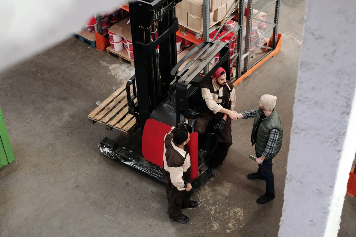 Overhead view of warehouse workers beside a forklift and wooden pallets.