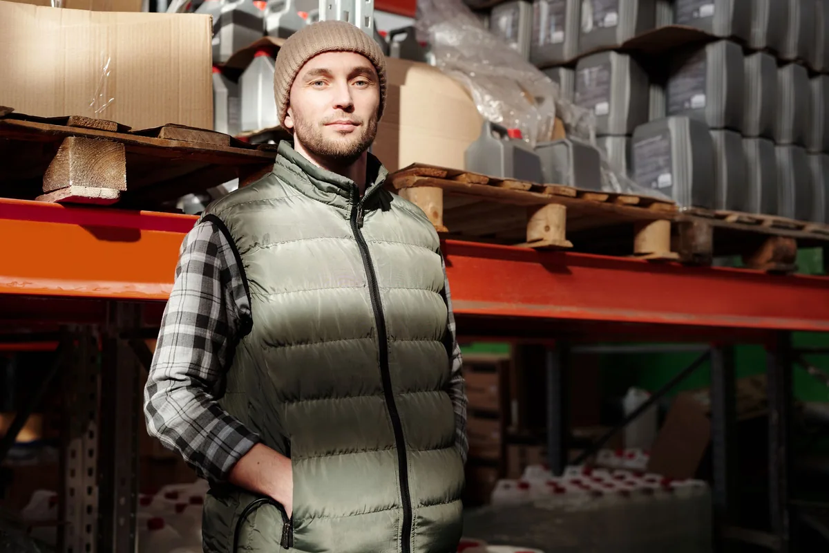 Warehouse worker standing beside stored goods and pallet racks.