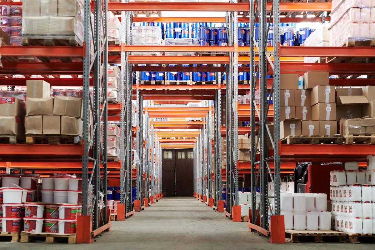 Warehouse aisle lined with pallet racks holding boxed goods and supplies.